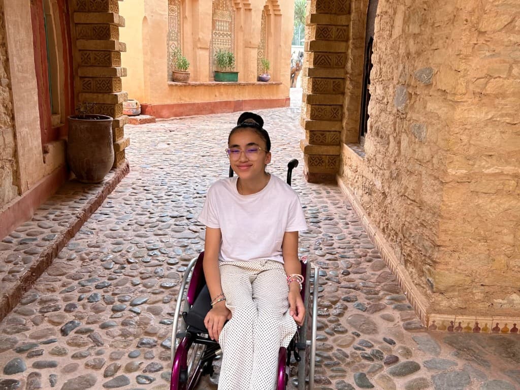 Inaya, sourire au premier plan, dans une ruelle ensoleillée